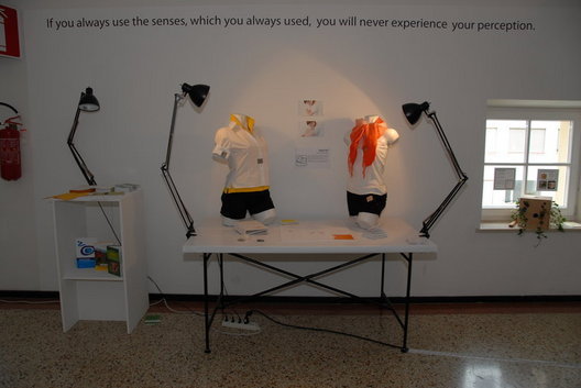 Eine Ausstellung mit zwei beleuchteten Schaufensterpuppen, die Sportkleidung tragen, auf einem Tisch, begleitet von einem Motivationszitat an der Wand.